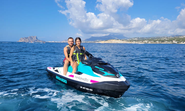 Una pareja en una moto de agua con vistas a la costa rocosa.