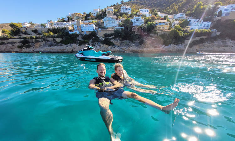Dos personas flotando en el agua junto a una moto de agua.
