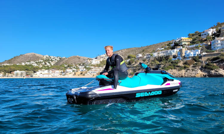 Una persona en una moto de agua con casas en la colina al fondo.